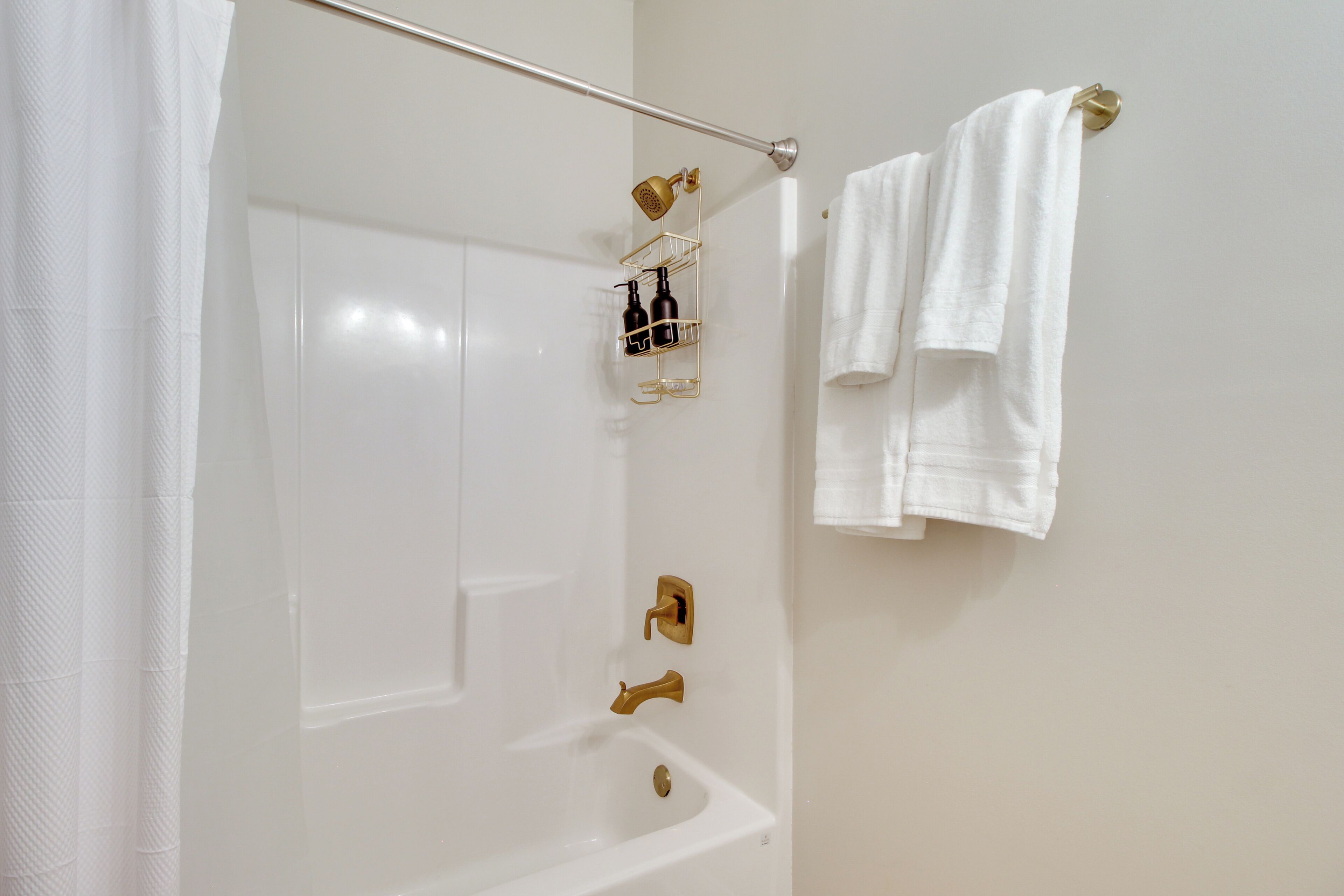 A bathroom with a white bathtub, a gold showerhead, and a towel rack with two towels.