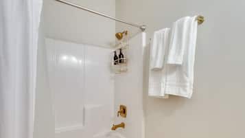 A bathroom with a white bathtub, a gold showerhead, and a towel rack with two towels.