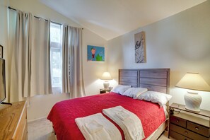 A hotel room with a large bed, two bedside lamps, a painting on the wall, and a window with curtains.