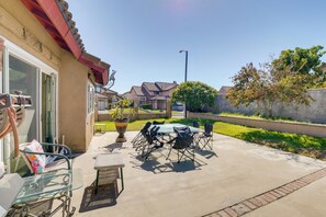 An outdoor patio area with a glass table and chairs, a potted plant, and a view of neighboring houses.