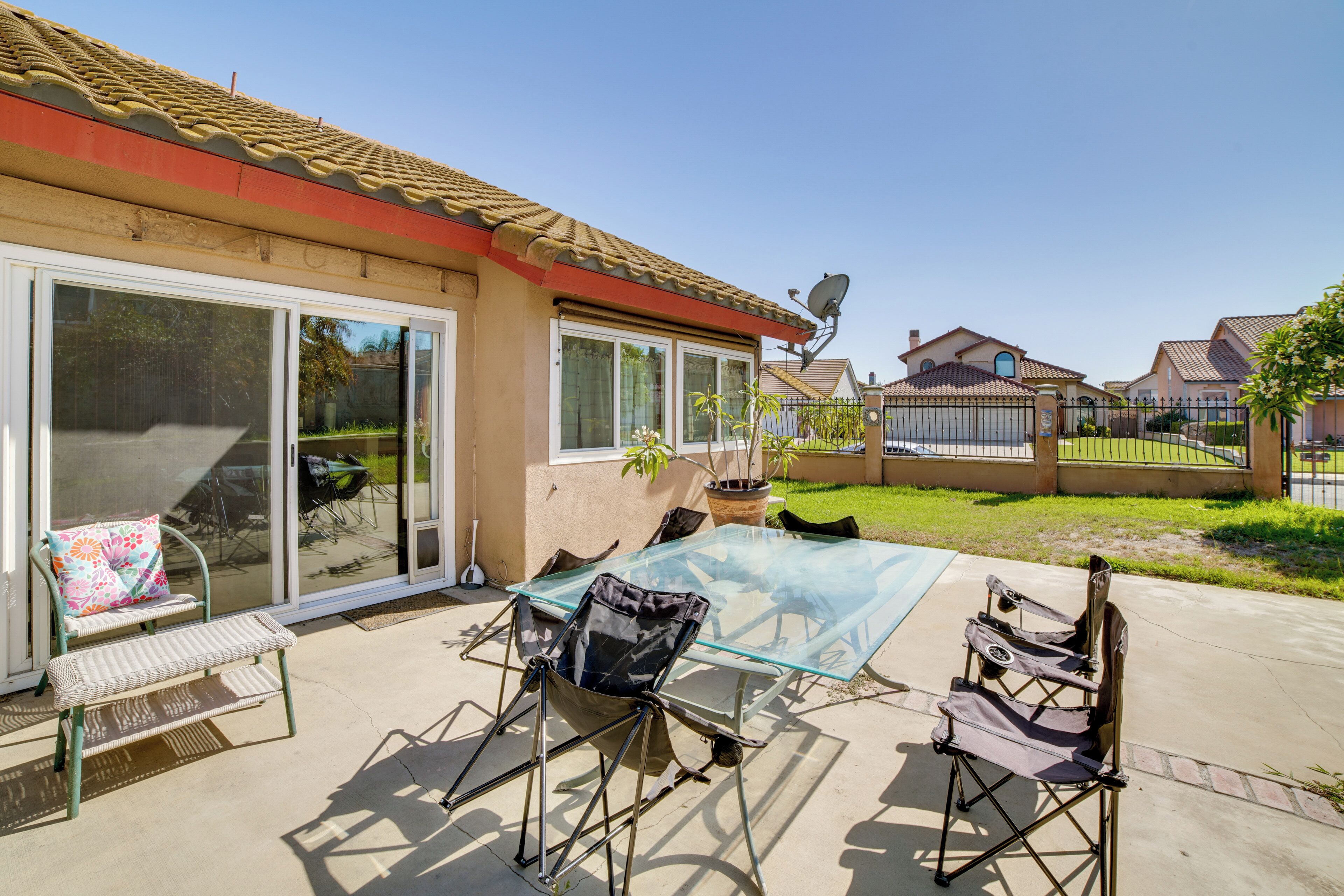 Eine Terrasse mit einem Glastisch, Stühlen, einer Bank und einer Glasschiebetür zu einem überdachten Außenbereich.