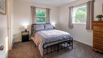 A bedroom with a bed, bedside tables, a dresser, and two windows with curtains.