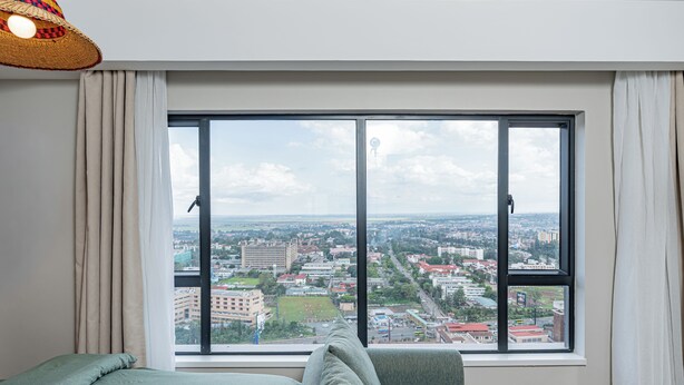 A hotel room with a large window, a bed, a chair, and a hanging light fixture. - Stylish Studio apartment Upperhill｜Pool & Gym (Nairobi)