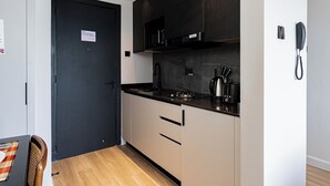 A compact kitchen with a black door, a coffee machine, and a telephone on the wall. - Stylish Studio apartment Upperhill｜Pool & Gym (Nairobi)