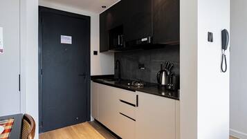 Une petite cuisine avec une porte noire, une machine à café et un téléphone fixé au mur.