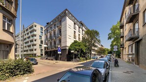 A street view with multi-story buildings, parked cars, and a clear sky. - Modern Apartment With a Balcony | Air Conditioning (Kraków)