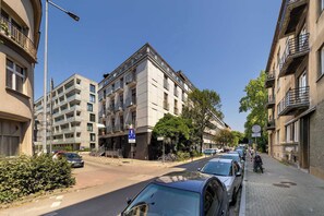 Straßenansicht mit mehrstöckigen Gebäuden, parkenden Autos und blauem Himmel.