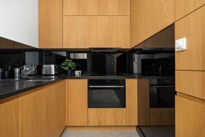 Een moderne keuken met houten kastjes, een zwart aanrecht, roestvrijstalen apparatuur en een inbouwvaatwasser.