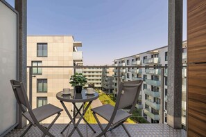 Ein Balkon mit Tisch und Stühlen, einem Blumentopf und Blick auf benachbarte Gebäude.
