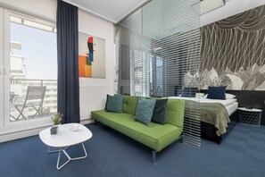 Een moderne hotelkamer met een groene bank, een klein wit tafeltje en een bed met een gestreept hoofdeinde.