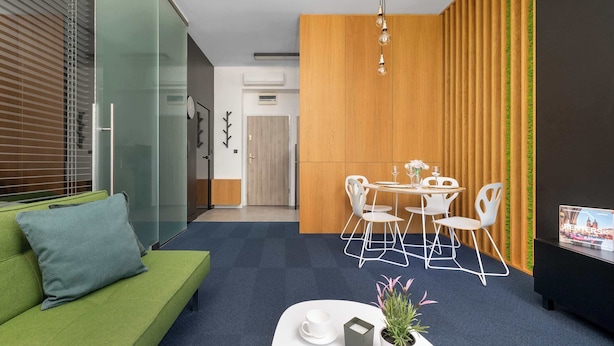 A modern living space with a green sofa, a dining area with white chairs, and a television screen displaying an image. - Modern Apartment With a Balcony | Air Conditioning (Kraków)