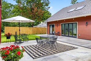 Un patio con alfombra de exterior a cuadros, sillas de metal y una mesa.