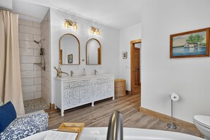 Un baño con ducha, un tocador blanco con dos espejos y un cuadro en la pared.