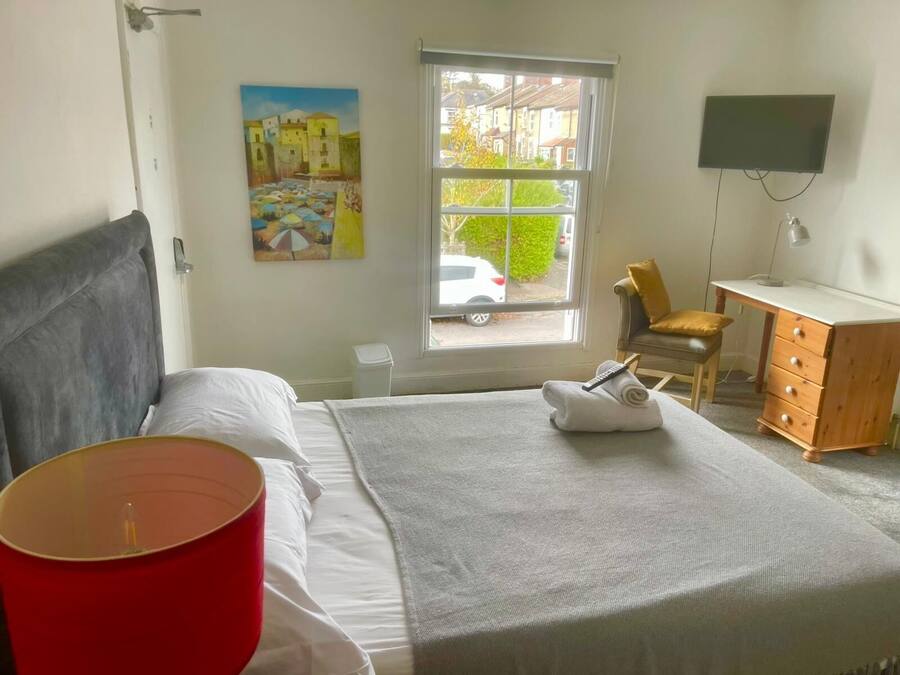 Ein Schlafzimmer mit einem Bett, einem Schreibtisch, einem Stuhl, einem Fernseher und einem Fenster mit Blick auf eine Straße.