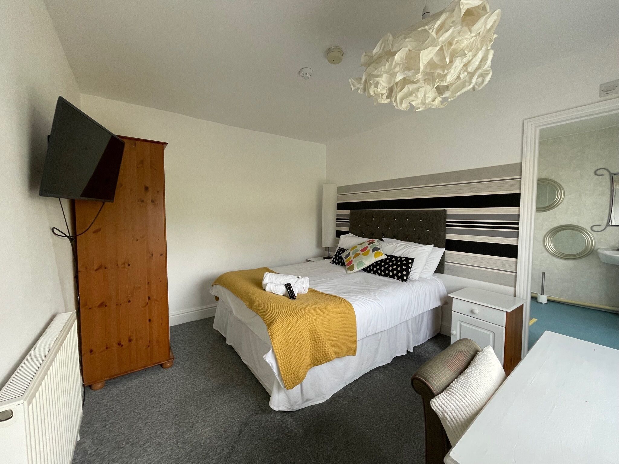 Habitación de hotel con cama, escritorio, armario, televisor montado en la pared y lámpara del techo.