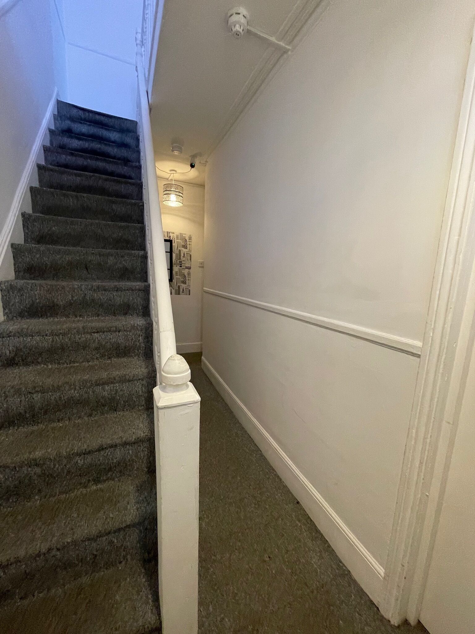 Una escalera con barandilla, peldaños alfombrados y una pared blanca con una puerta al final.