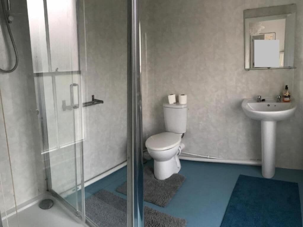 A bathroom with a glass shower enclosure, a white toilet, a sink, and a mirror.