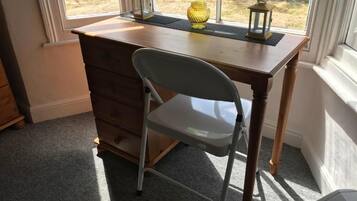 Un escritorio con una silla, una ventana que ofrece vistas al exterior, y un pequeño florero amarillo sobre el escritorio.