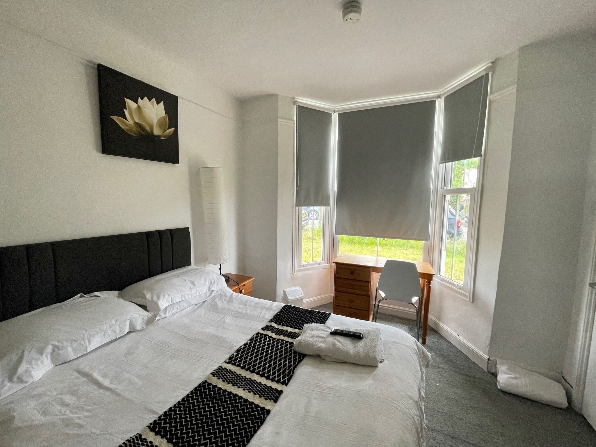 Ein Hotelzimmer mit einem großen Bett, einem Schreibtisch und einem Stuhl. Es gibt ein Fenster mit Vorhängen und Blick nach draußen.