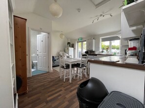 A compact kitchen with a dining area, wooden flooring, and a white door leading to a bathroom. - Golden Triangle Rooms (Norwich)