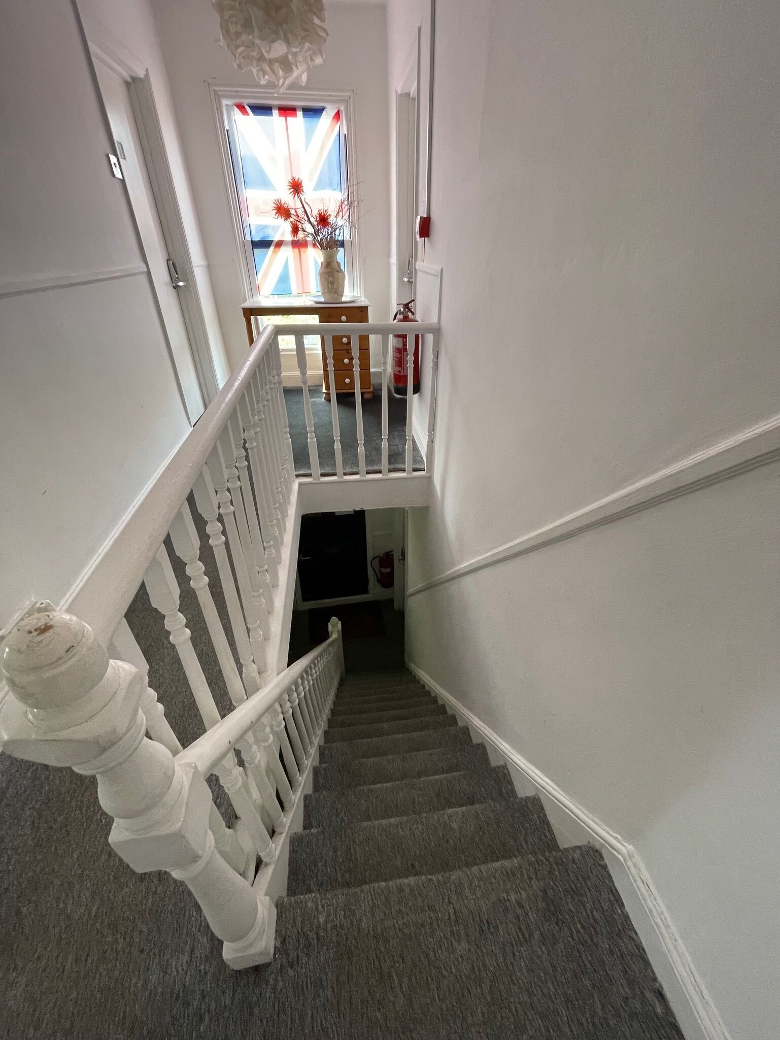 A staircase with white balusters and a handrail, leading to a landing with a table and vase.