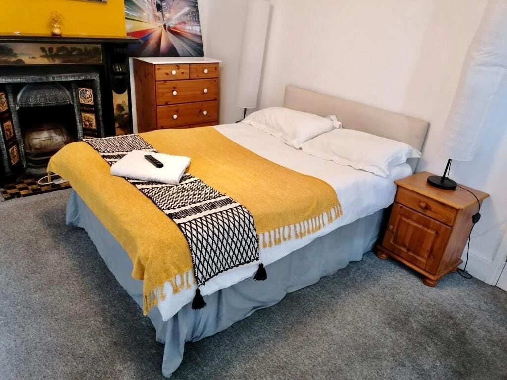 A bedroom with a bed, a nightstand, a dresser, and a fireplace.