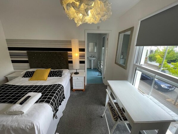 A hotel room with a bed, bedside table, desk, and a view of the street.