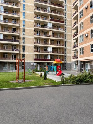 Un immeuble résidentiel à plusieurs étages doté de balcons, d’une aire de jeux avec un toboggan et une balançoire.