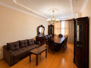 Ein Wohnzimmer mit einer Couch, einem Esstisch mit Stühlen, einer Chandelüster und einer großen Holzkommode.