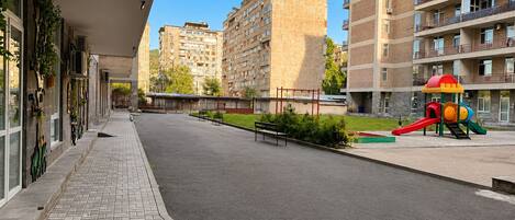 A pedestrian walkway with a playground, benches, and a building with multiple floors.