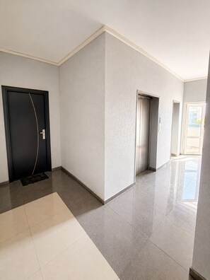 A hallway with a black door, a white wall, and a tiled floor.