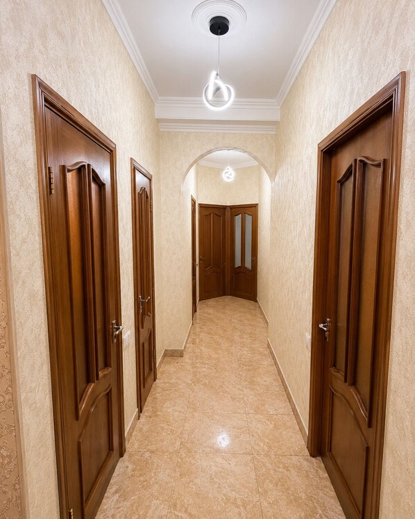 Un couloir avec des portes en bois, un sol carrelé et un luminaire au plafond.