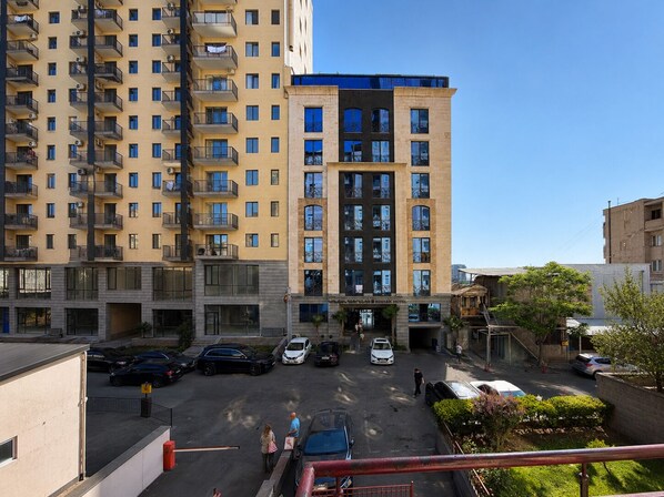 Un hotel de varios pisos con un estacionamiento al frente, que presenta un edificio moderno con balcones y un cielo despejado.