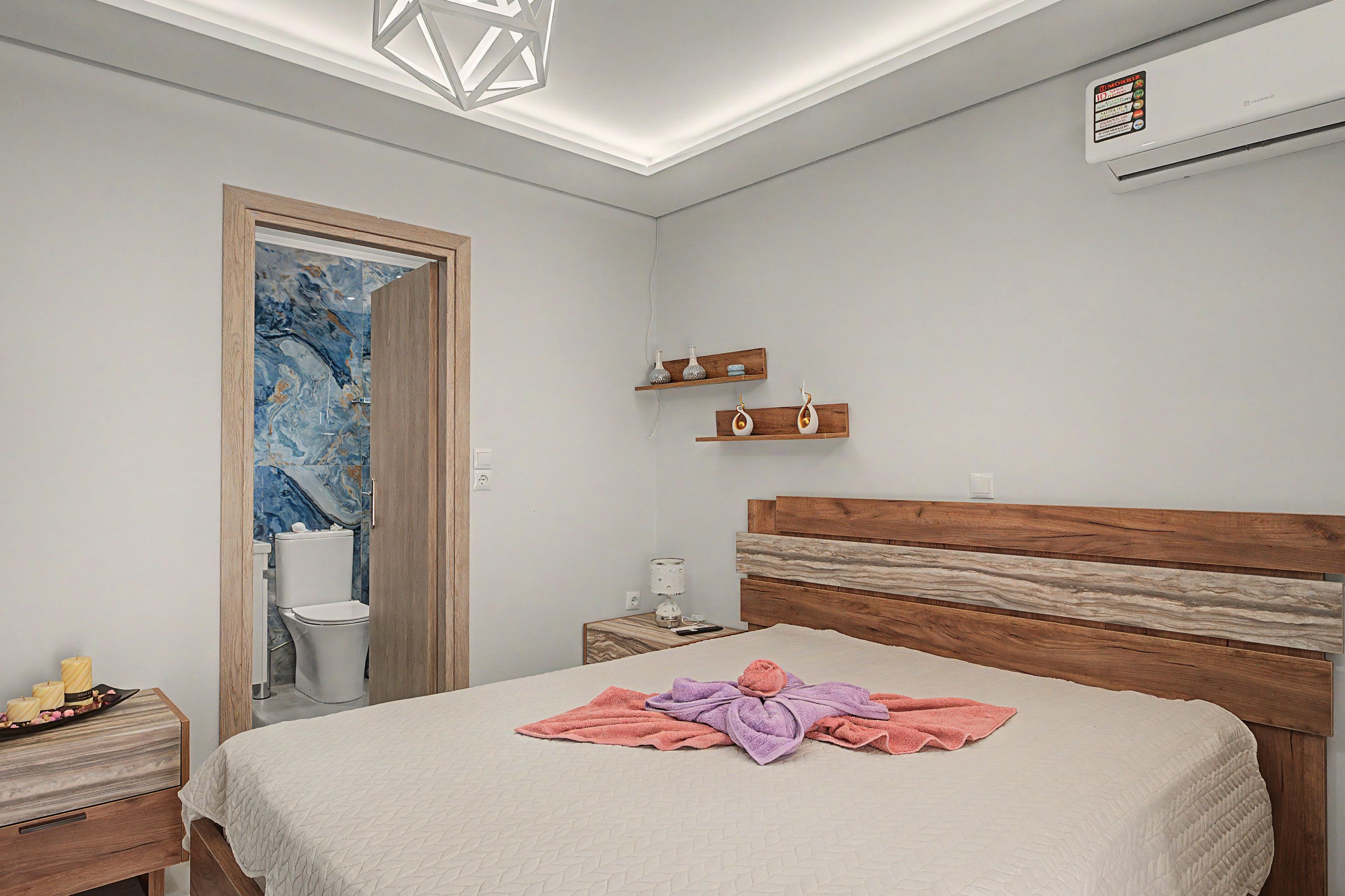 Een slaapkamer met een bed, nachtkastje, wandairconditioning en een nachtlampje.