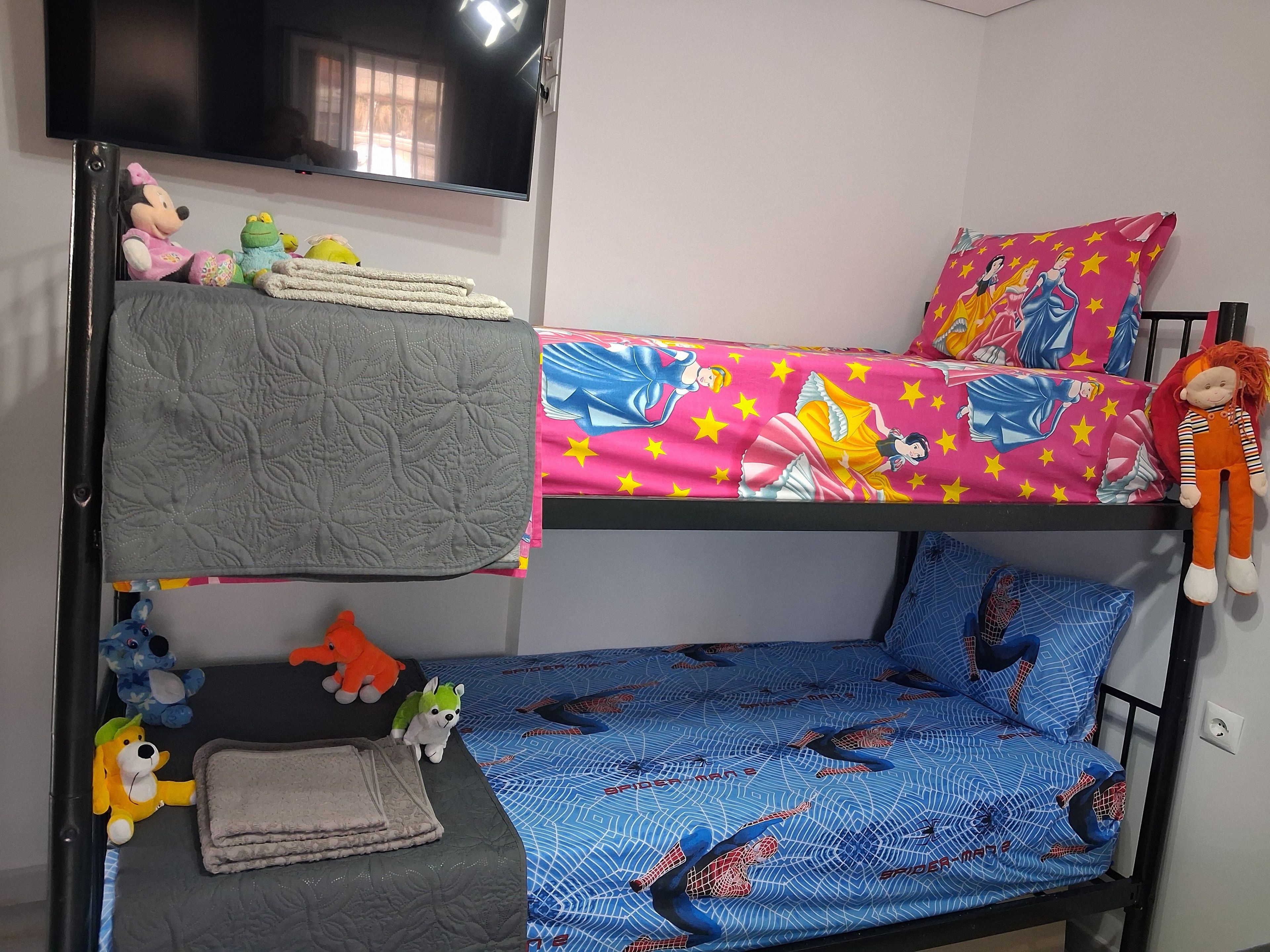 A bunk bed with a TV mounted above, plush toys on the beds, and a Spider-Man themed bedspread.