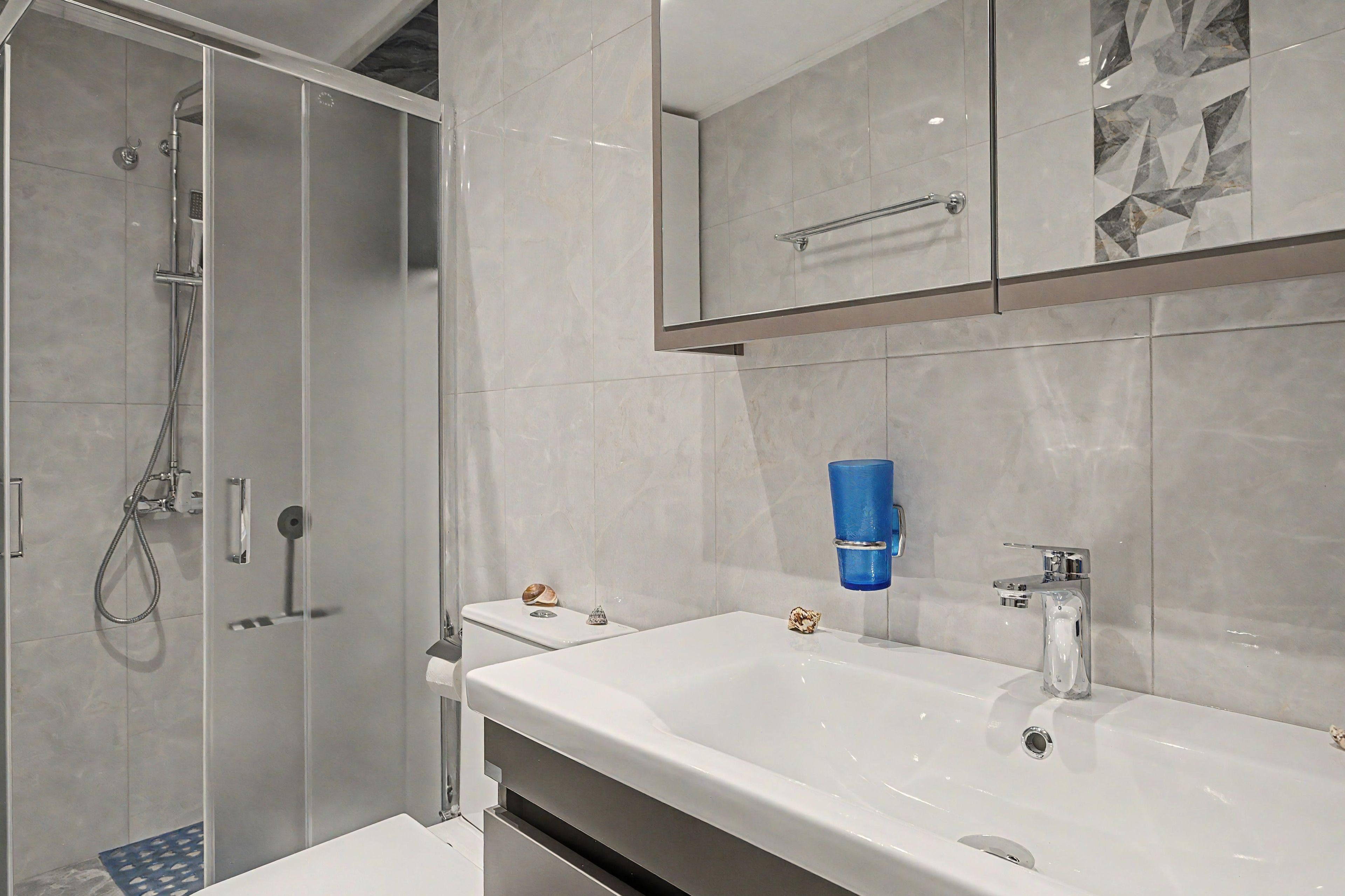 Une salle de bain moderne avec une douche à parois de verre, un lavabo blanc doté d’un robinet chromé et des carreaux à motifs de marbre.