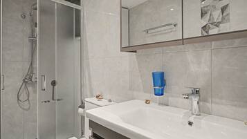 Une salle de bain moderne avec une douche à parois de verre, un lavabo blanc doté d’un robinet chromé et des carreaux à motifs de marbre.