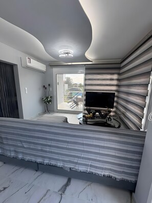 A modern living room with a sofa, a flat-screen TV, and a large window.