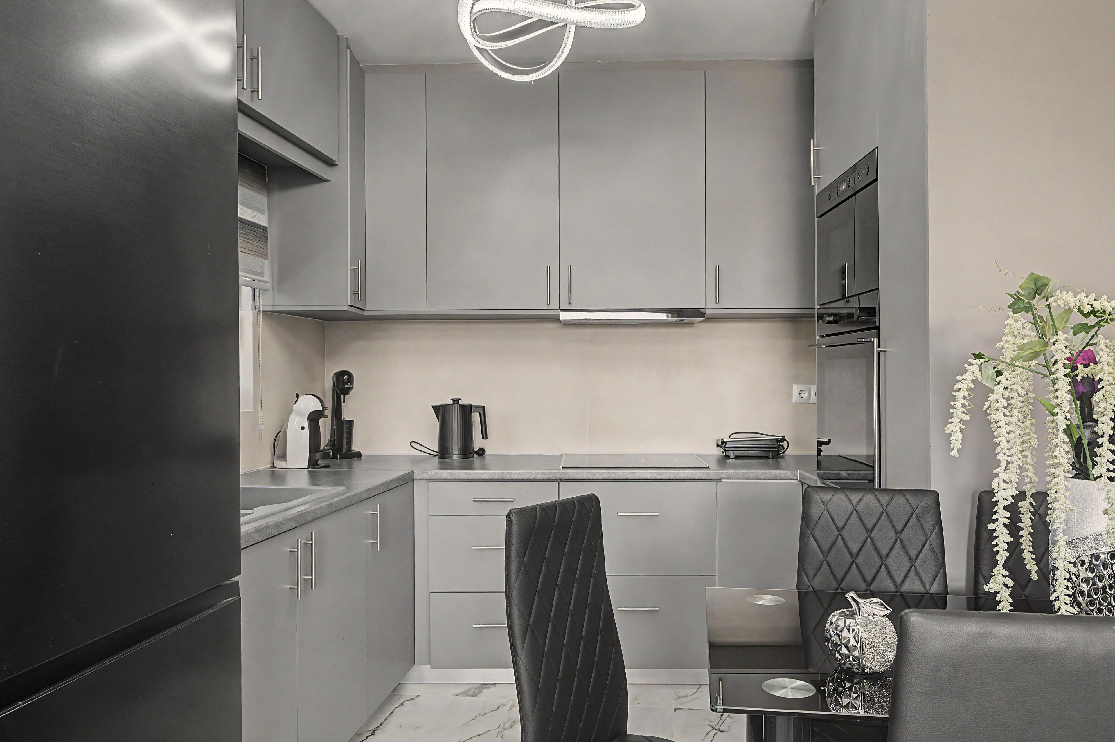 Una cucina moderna con mobili grigi, un piano di lavoro nero e un'area pranzo con una sedia e un tavolo neri.
