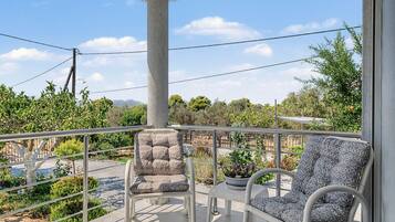 A balcony with two chairs and a table, overlooking a garden with various plants and a distant mountain range.