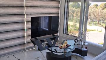 A modern living room with a flat-screen TV, a glass coffee table, and a sofa.