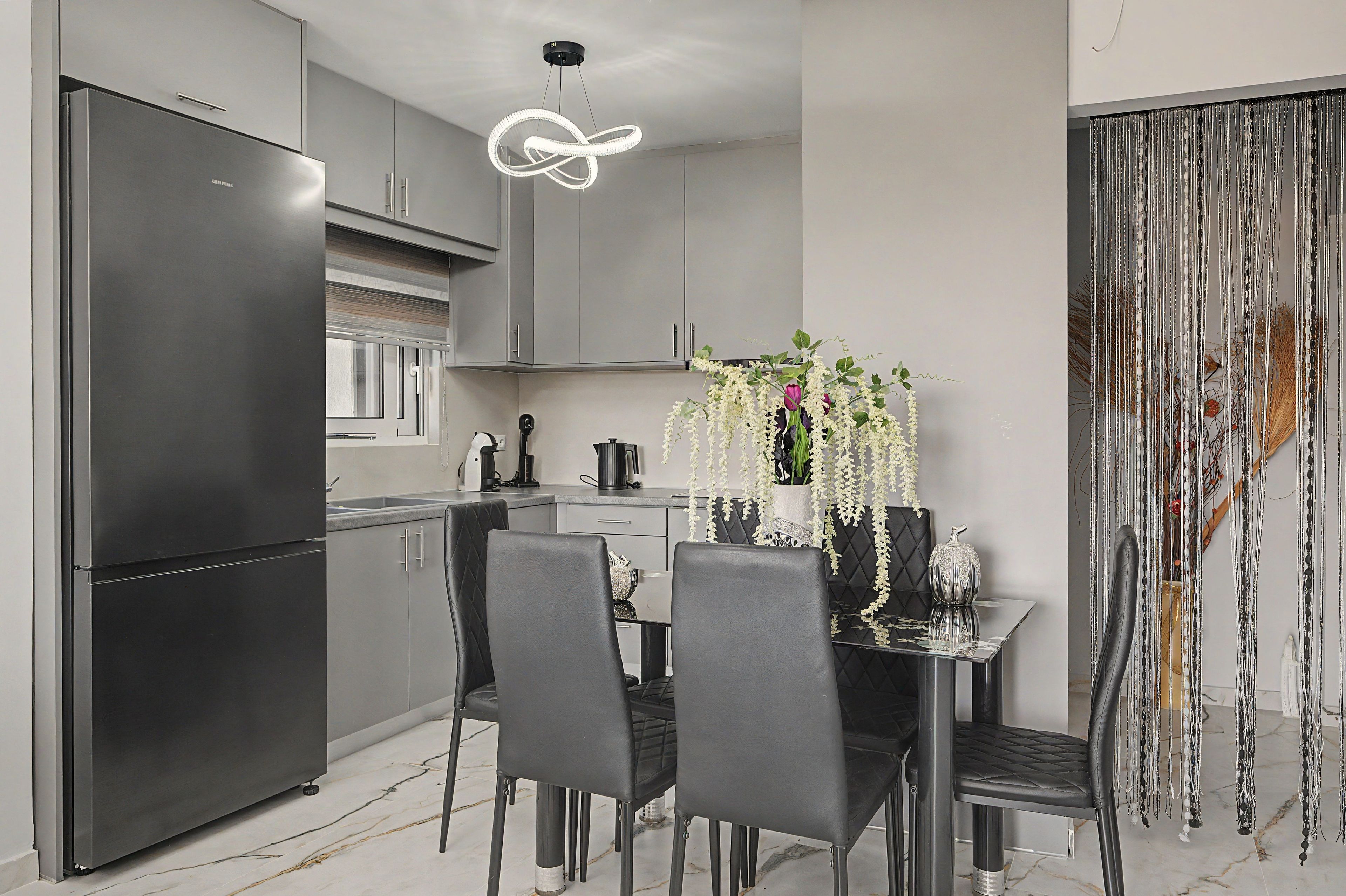 A modern kitchen with a built-in refrigerator, a dining table with chairs, and a hanging light fixture.