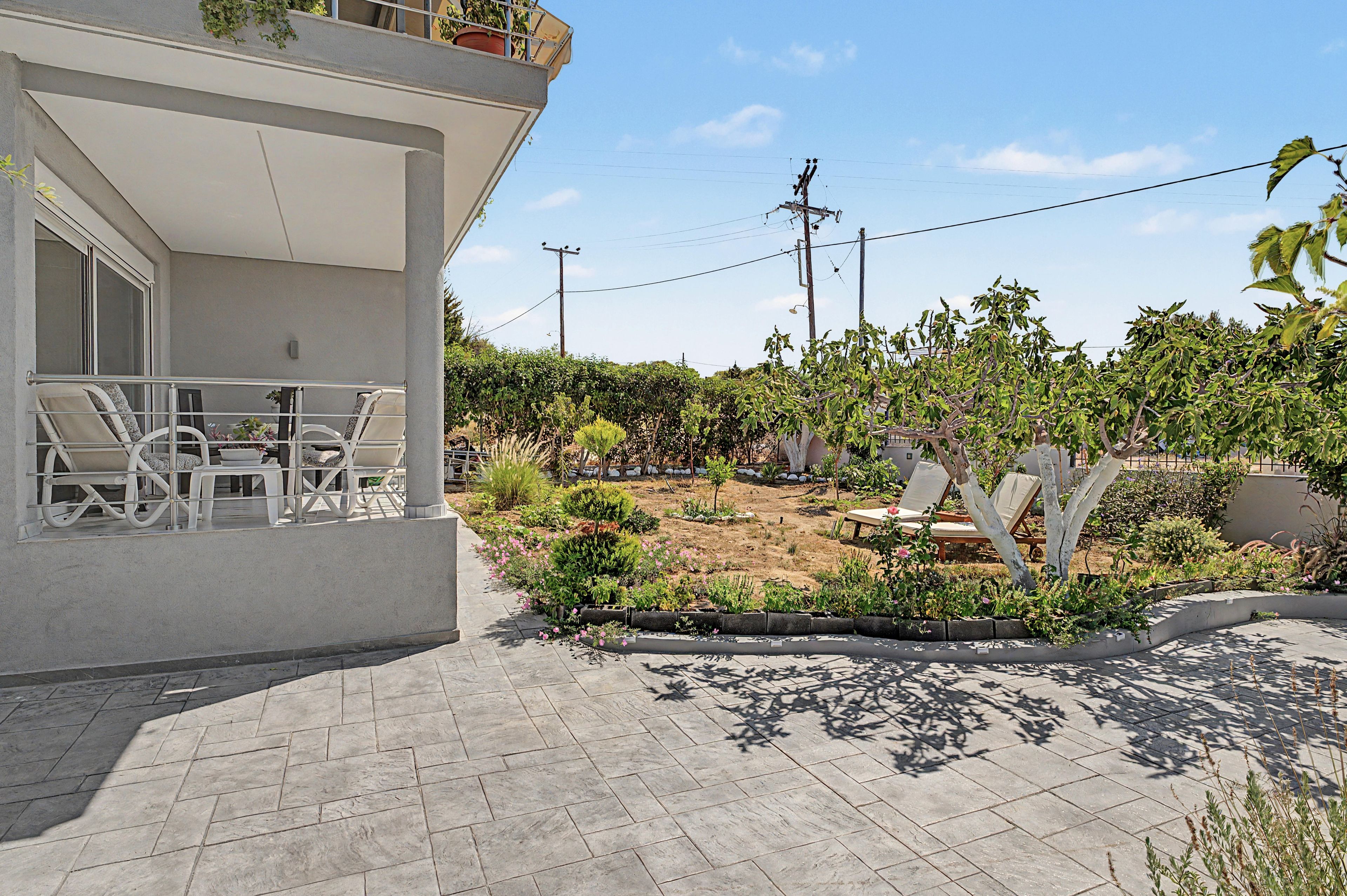 Een woonhuis met een terras, zitgedeelte buiten en een tuin met verschillende planten en bomen.