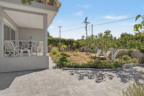 Il s'agit d'une propriété résidentielle dotée d'une terrasse dallée, d'un espace salon extérieur et d'un jardin agrémenté de diverses plantes et arbres.