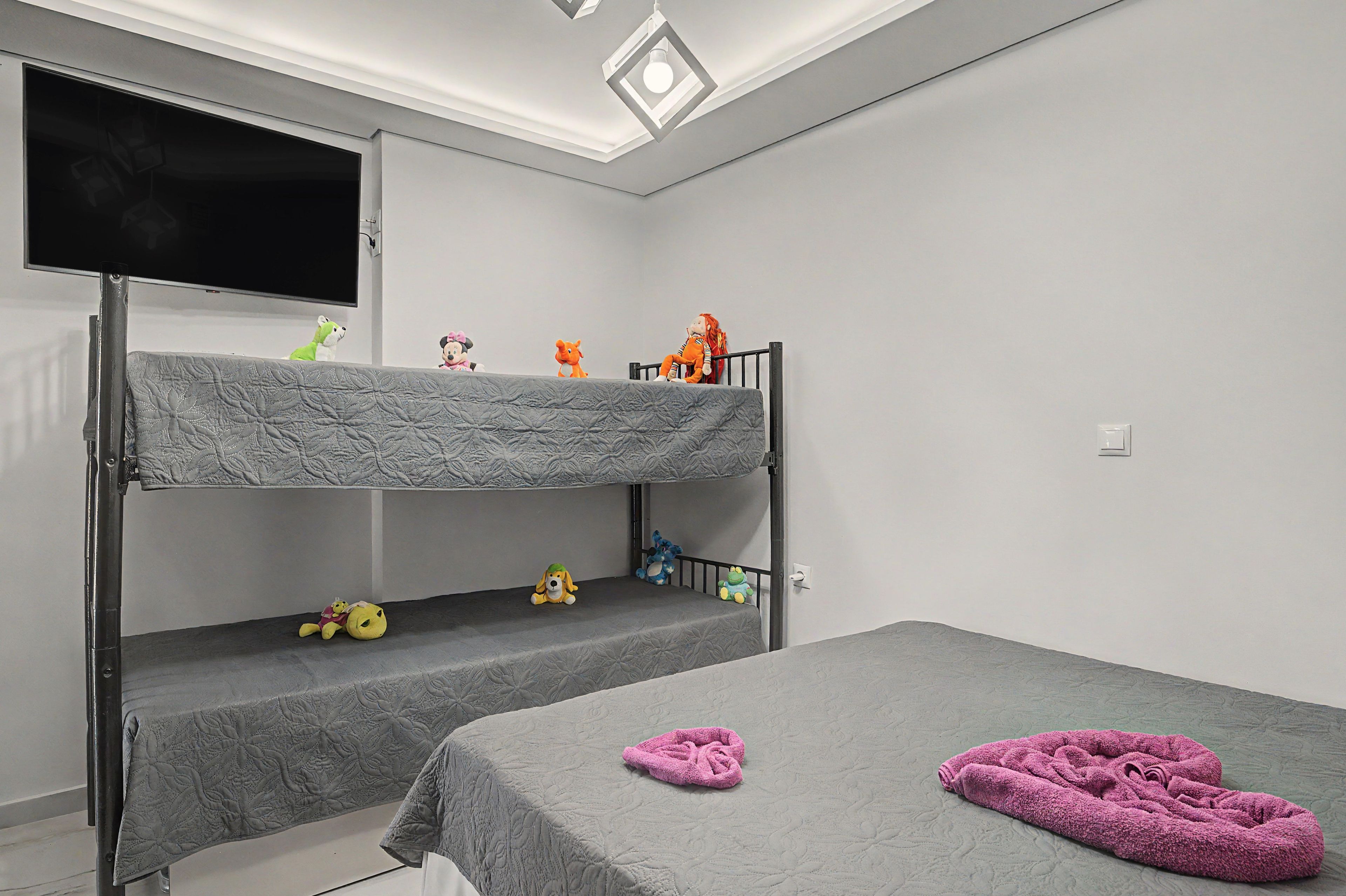 A bunk bed room with a flat-screen TV, plush toys, and a pink towel.