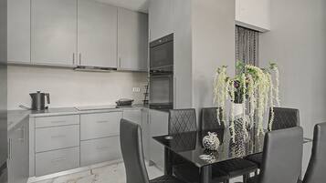 A modern kitchen with grey cabinets, a built-in oven, and a dining area with a black table and chairs.