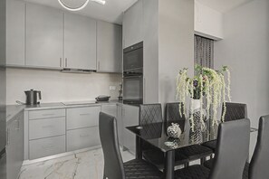 A modern kitchen with grey cabinets, a built-in oven, and a dining area with a black table and chairs.