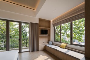 A modern interior with large windows, a built-in bench, and a flat-screen TV. - Cove Svasa (Jakarta)