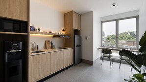 A modern kitchen with wooden cabinets, a stainless steel refrigerator, a microwave, and a sink. There is a window providing a view of the outside. - Cove Svasa (Jakarta)
