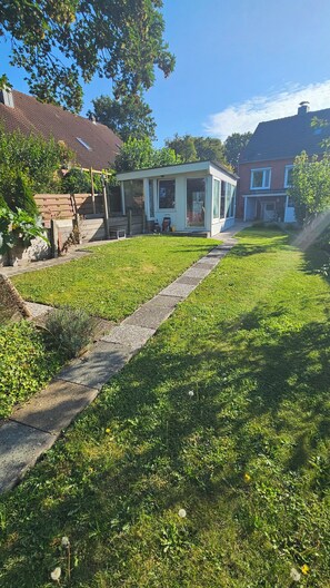 Een woonhuis met een verzorgd gazon, een kleine tuinhuisje en een rietgedekte woning van baksteen.